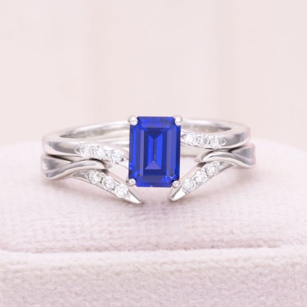 The straight lines of this emerald cut lab-created sapphire are balanced by the gentle curves of the slightly offset bands in this striking bridal set. We set a handful of diamond accents into both the bands, adding a touch of bling and tying the two bands together.