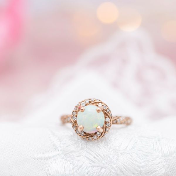 Rose gold engagement ring with a white opal center stone and twisting halo.
