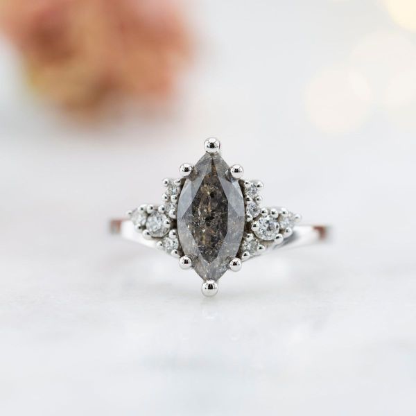 A marquise cut salt and pepper diamond in deep gray is flanked by white diamond accents in a white gold setting.