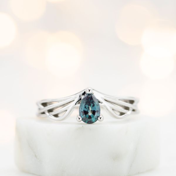 精致，现代的订婚戒指与翅膀一样的曲线框架梨切翠绿宝石。