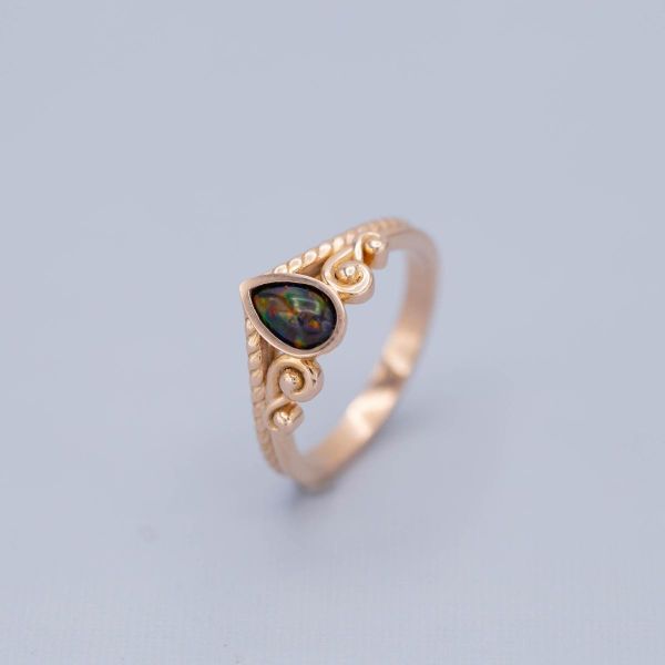 This antique-inspired ring surrounds a colorful black opal with rose gold scrollwork.