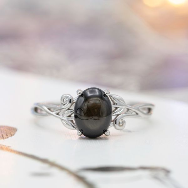 Black star sapphire engagement ring with a delicate, leafy white gold setting.