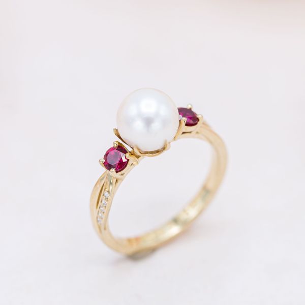 时尚和引人注目!这枚由三颗宝石组成的戒指两侧的红宝石与中间的珍珠相映成辉。