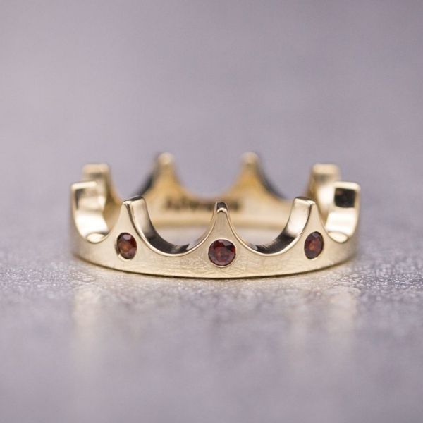 A subtle, modern tiara ring in rose gold with minimal ornamentation and flush-set red garnets.