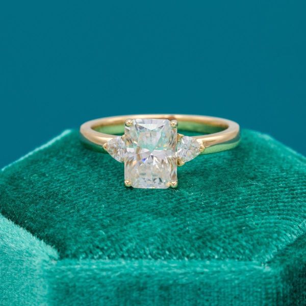 A classic three-stone yellow gold and moissanite engagement ring with radiant and trillion cut stones.