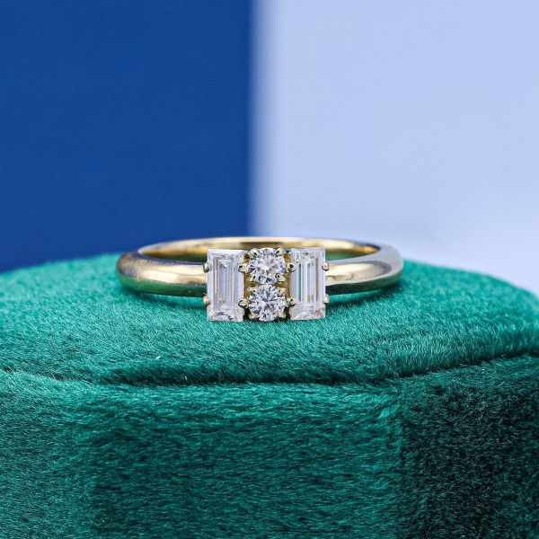 Two vertical-set round moissanites are guarded on either side by a baguette cut moissanite on this yellow gold engagement ring.