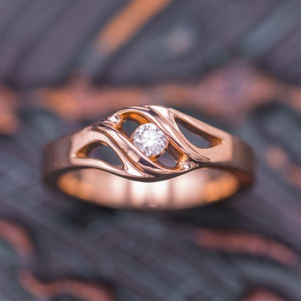 A wider rose gold band appears to stretch into organic, curving openings, allowing light to pass and nestling a diamond center stone.