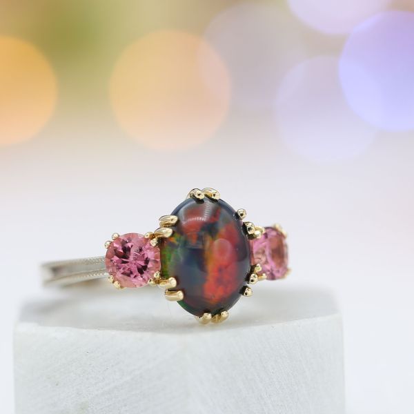 黑色蛋白石和粉红色碧玺订婚戒指与双尖头和米格纹边带。