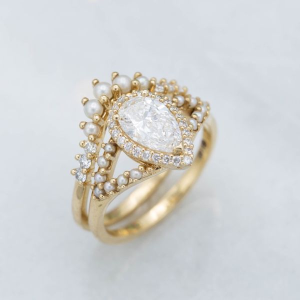 0.9克拉梨形钻石镶嵌在14k金半柄光环订婚戒指上，搭配一枚轮廓鲜明的珍珠婚戒。