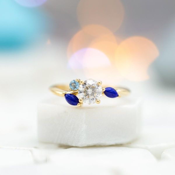 这枚以水为灵感的订婚戒指上，青金石和海蓝宝石不对称地围绕着钻石。