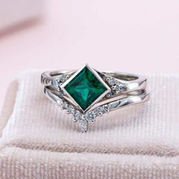 A princess cut emerald sits in the center of this tiara inspired bridal set.