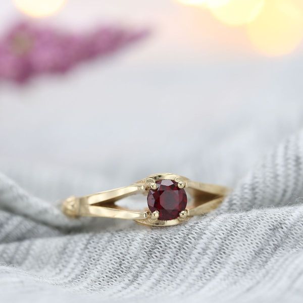 A deep red ruby sits atop golden snitch-like wings in this yellow and white gold engagement ring.