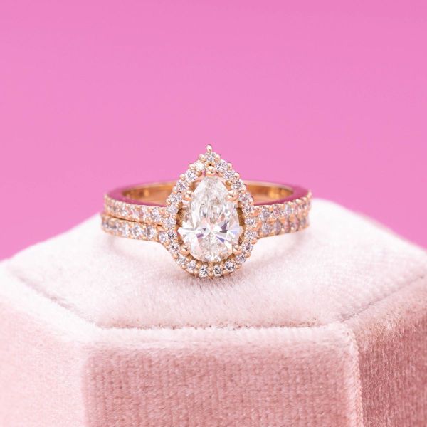 A halo of pavé-set diamond accents dance around this engagement ring’s pear cut diamond as more grace the matching wedding band.