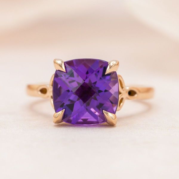 Rose gold claw prongs hold a cushion cut amethyst in this solitaire engagement ring.