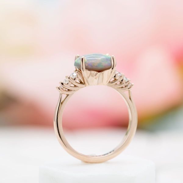 An oval cut opal sits in an east-west setting on this rose gold engagement ring.