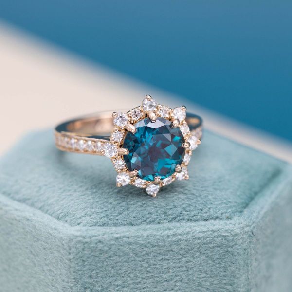 A teal blue alexandrite is surrounded by a sunburst of moissanites in this engagement ring.