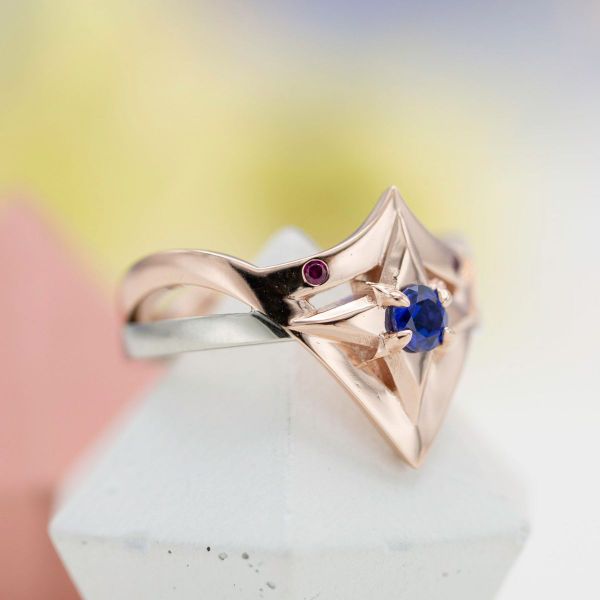 A lab created sapphire pops on this Wonder Woman’s headpiece inspired engagement ring.
