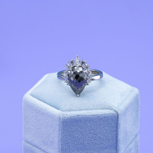 A pear shaped salt and pepper diamond has a unique half halo of additional diamonds.