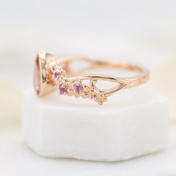 An amethyst sits on this rose gold band with darker amethyst accent stones set in a floral formation.