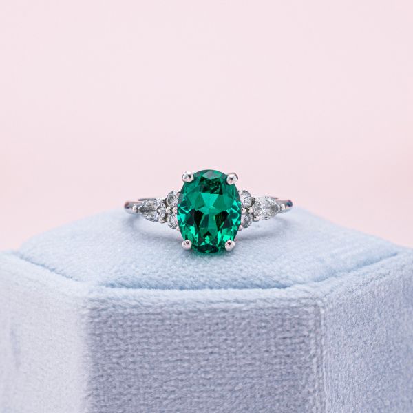 A lab created emerald in an oval cut sits in button prongs of white gold.