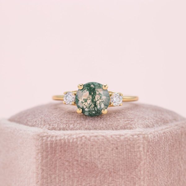 A round moss agate sits in the center of the yellow gold engagement ring flanked by diamond accents.