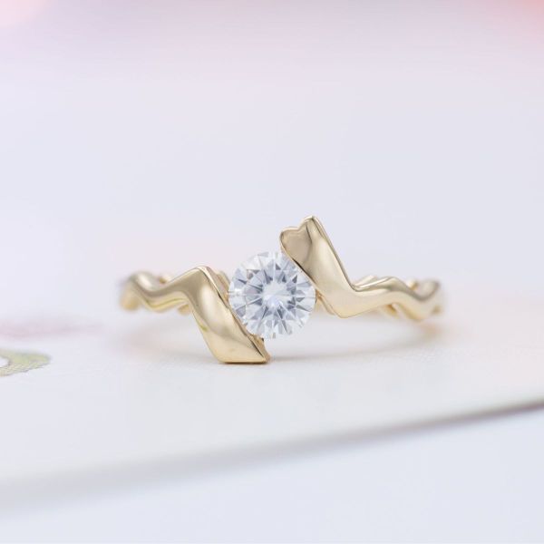 A lightning bolt shaped yellow gold band captures a brilliant round moissanite in the faux tension setting of this Pokémon-inspired engagement ring.