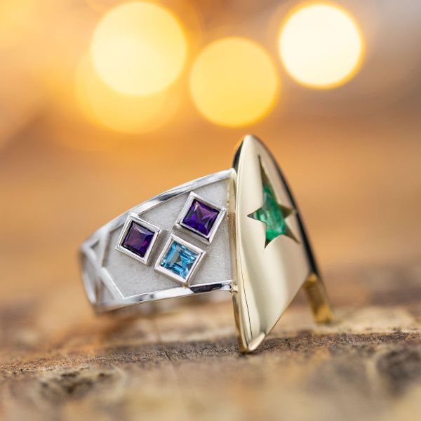 A large Star Trek inspired logo acts as a setting for the pear-cut emerald center stone.