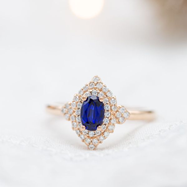 A classic, deep blue lab-created sapphire center stone set in a vintage-inspired halo engagement ring