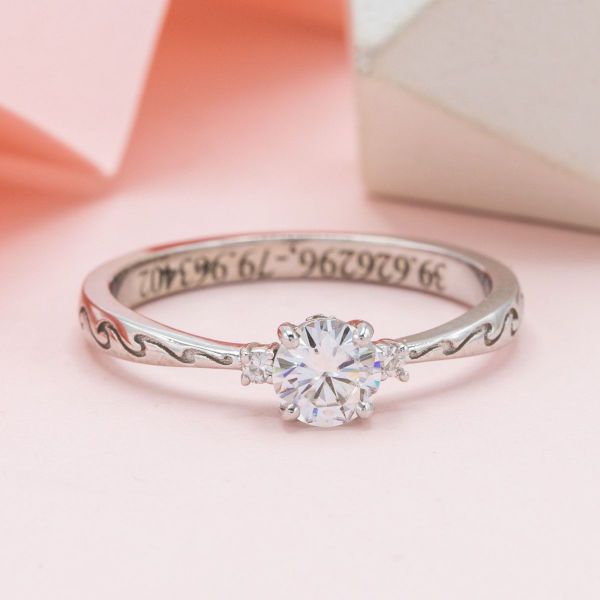 Moissanite is showcased in a white gold band with tiny waves engravings along the band of this ocean-inspired engagement ring