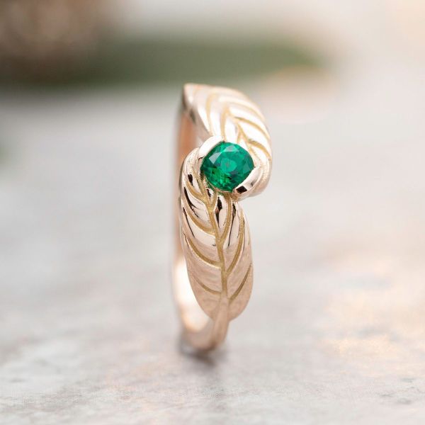 The rose gold band of this autumn-inspired engagement ring looks like leaves embracing the lab emerald center stone.