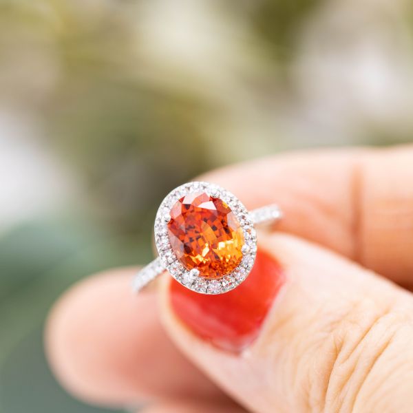 This lab-created sapphire's fiery orange captivates at the center of a sparkling halo.