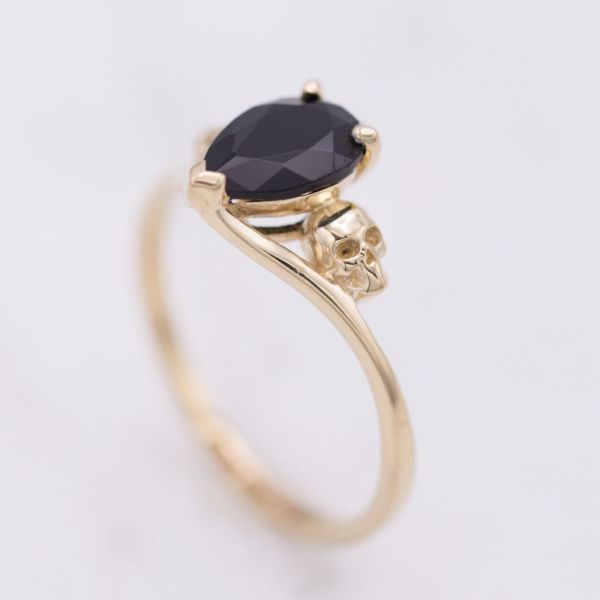 A delicate gold ring with subtle skulls tucked in the asymmetric curve of the band, just below the pear cut onyx.