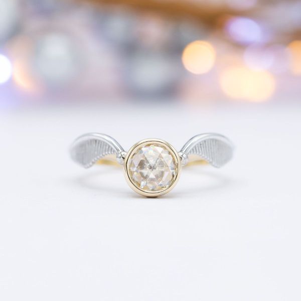 Two white gold wings flow from a beautiful rose-cut moissanite.