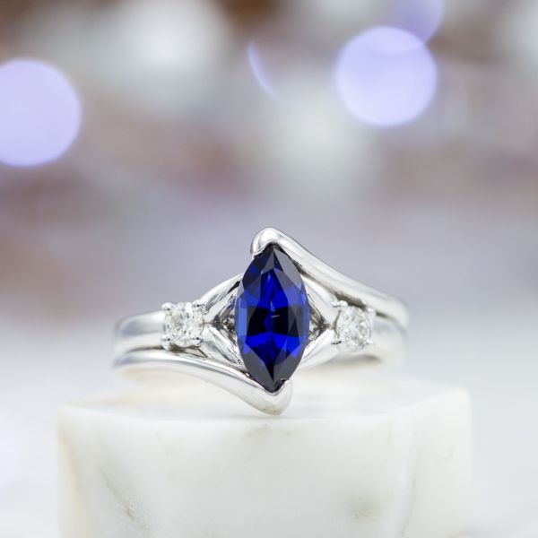 White gold engagement ring with bypass setting and accent diamonds around a lab-created marquise blue sapphire.