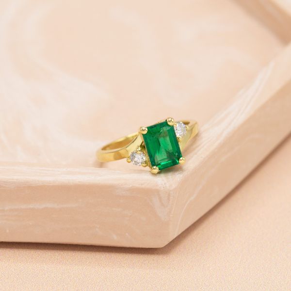 This natural mined emerald is flanked by diamond accents in a yellow gold faux tension setting.