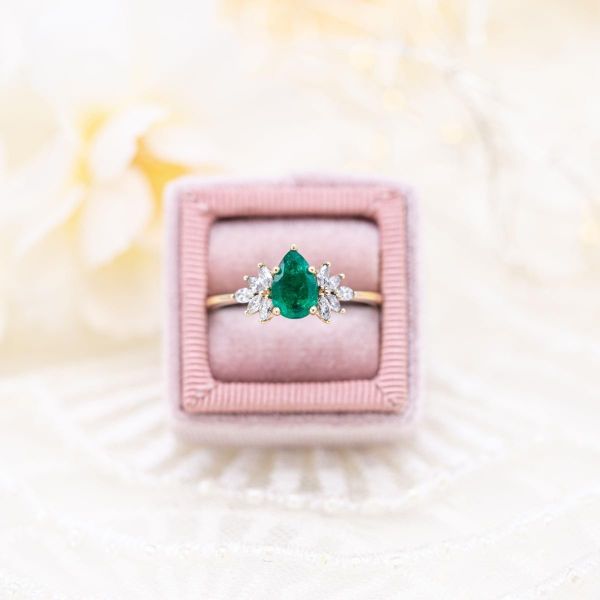 在这枚订婚戒指的中心，梨形祖母绿钻石的两侧呈扇形散开。
