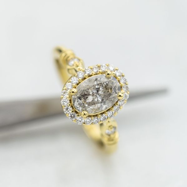 This oval diamond features beautiful black speckling on a translucent gray body, and brings a cool modern balance to the vintage elements of the ring's gold setting.