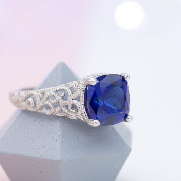 Vintage-inspired statement ring with milgrain-lined filigree and cushion cut blue sapphire center stone.