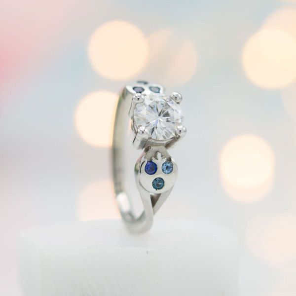 Rebel Alliance inspired logos with jewel accents flank the moissanite center stone in this Star Wars inspired engagement ring.