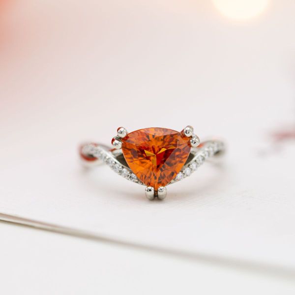 This timeless and unique engagement ring pairs a blazing orange trillion cut sapphire with a classic pavé diamond twisted band.