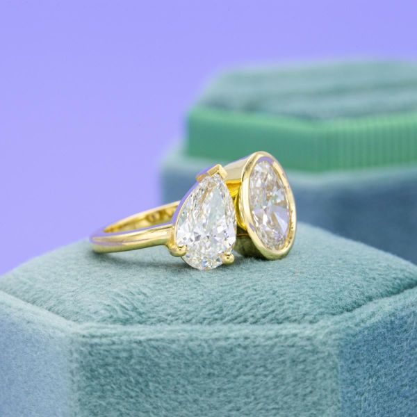 The two diamonds at the center of this yellow gold ring have a prong and bezel setting.