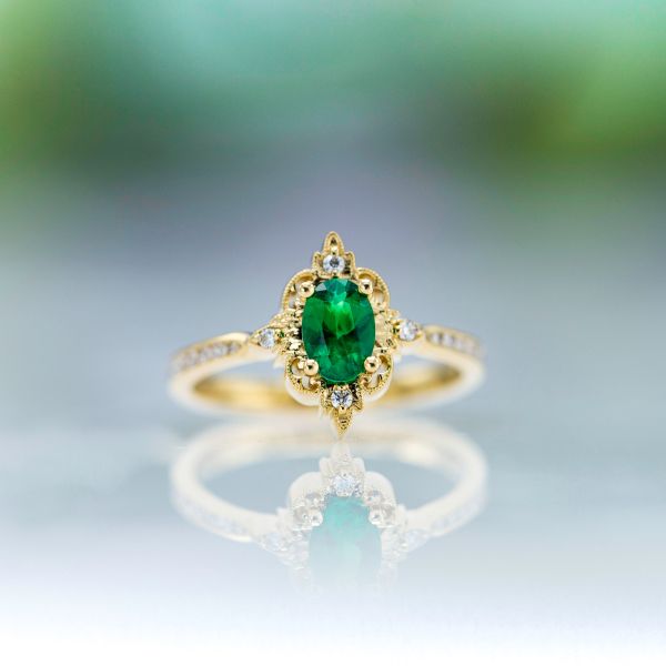 An oval cut emerald is an electric green in this antique frame and yellow gold style engagement ring.