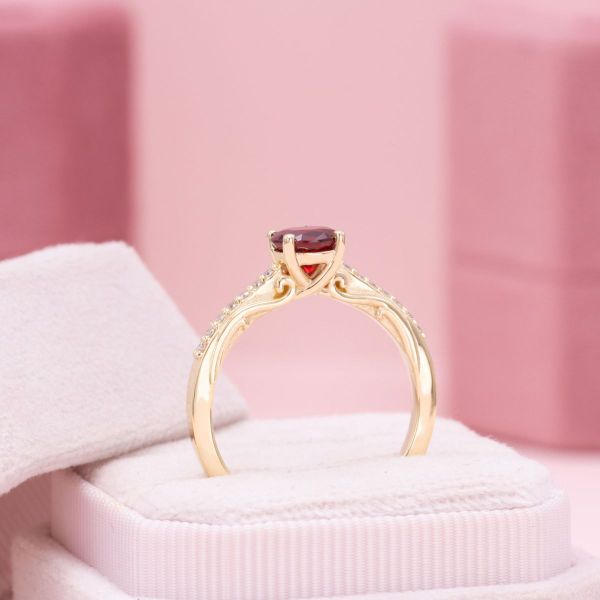 A ravishing ruby sits at the heart of this solitaire engagement ring with diamond accents and filigree decorating the yellow gold band.