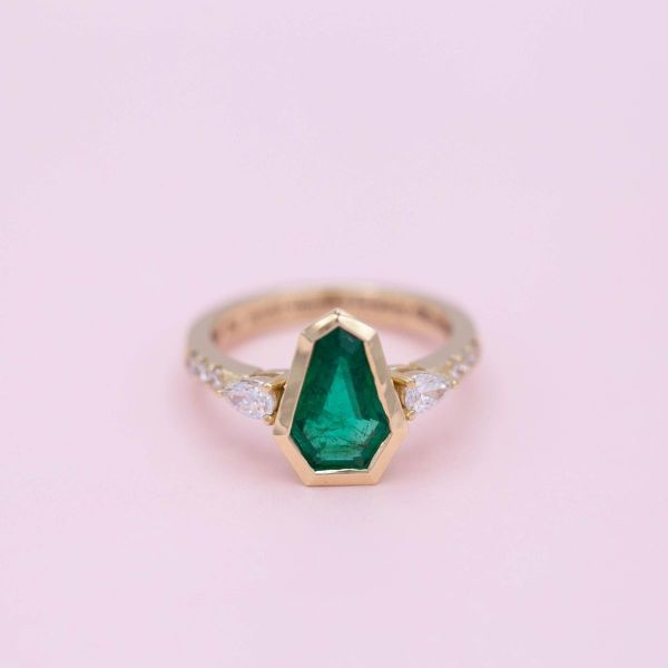 A custom coffin cut emerald center stone gives this ring a distinctive look.