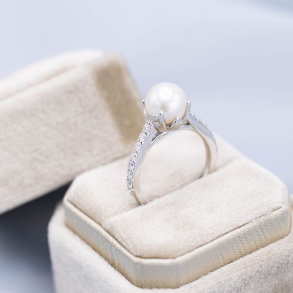 一枚干净而经典的珍珠订婚戒指，戒指上镶嵌着钻石，珍珠周围镶嵌着微妙的花卉。