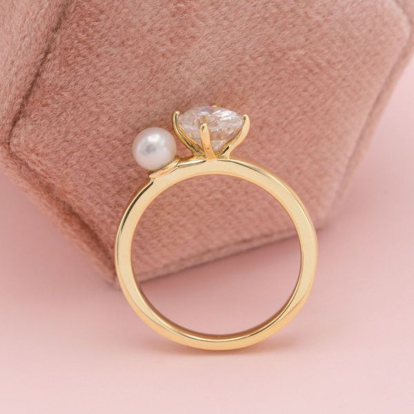 A pearl and oval cut moissanite sit in the center of this yellow gold toi et moi engagement ring.