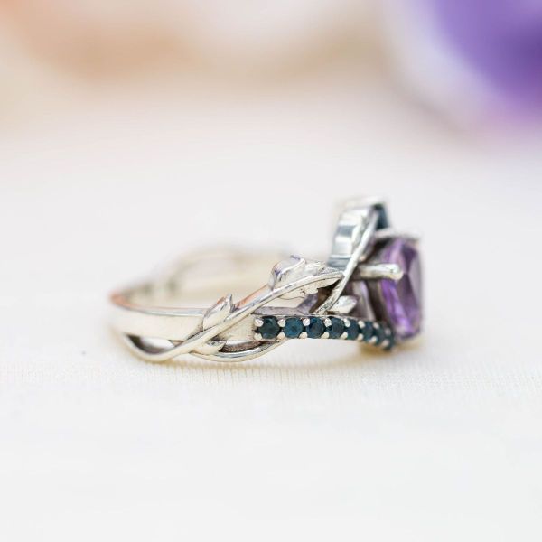 A wandering vine and blue topaz accents wind their way around the trillion cut amethyst center stone.