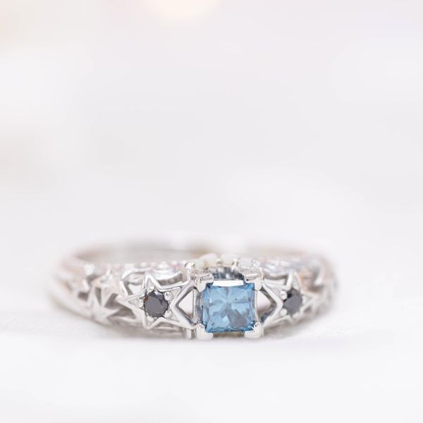 This teal blue diamond is paired with black and colorless diamond and white opal accents.