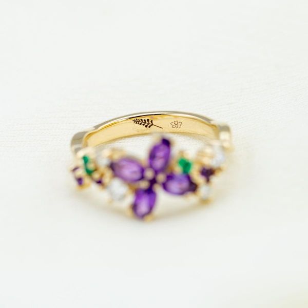This yellow gold ring has four amethysts at its center making up a lavender bloom with emerald and diamond accents.