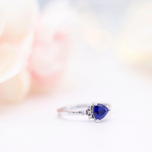 This ring's trillion cut sapphire is set in an east-west arrangement with a cluster of accent diamonds.